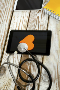 Doctor workplace with tablet and stethoscope on the sing of the heart, on wooden background