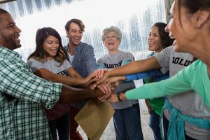 Diverse business colleagues put their hands together and cheer before beginning the volunteer assignment. They are participating in a team building outing.